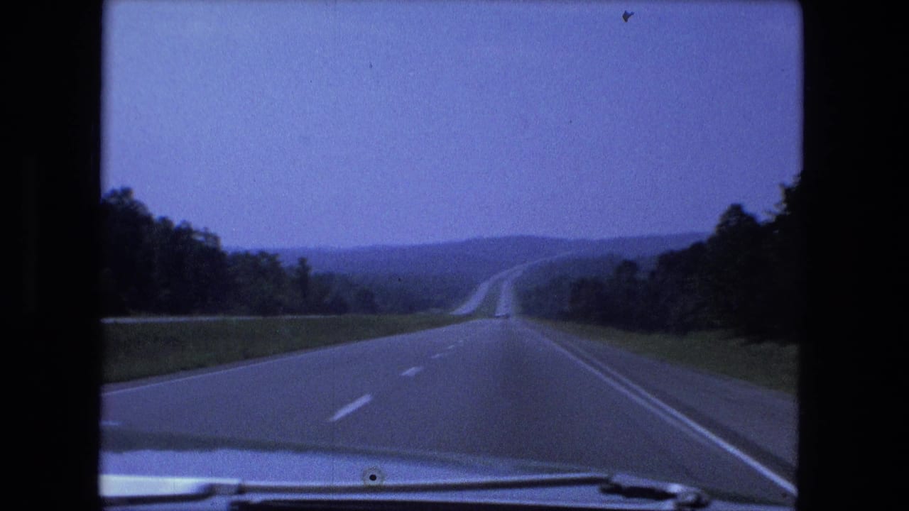 1974 8mm road-travel view near Fort Wayne, Indiana, with an open highway stretching into a green, wooded horizon.