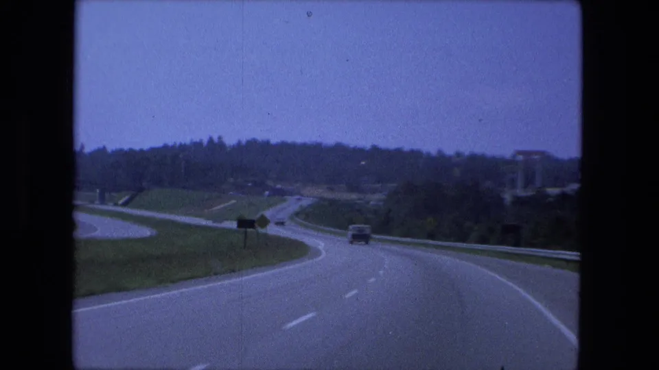 1974 Fort Wayne-area road scene showing a curving highway, junction lanes, guardrails, and sparse traffic from inside a car.