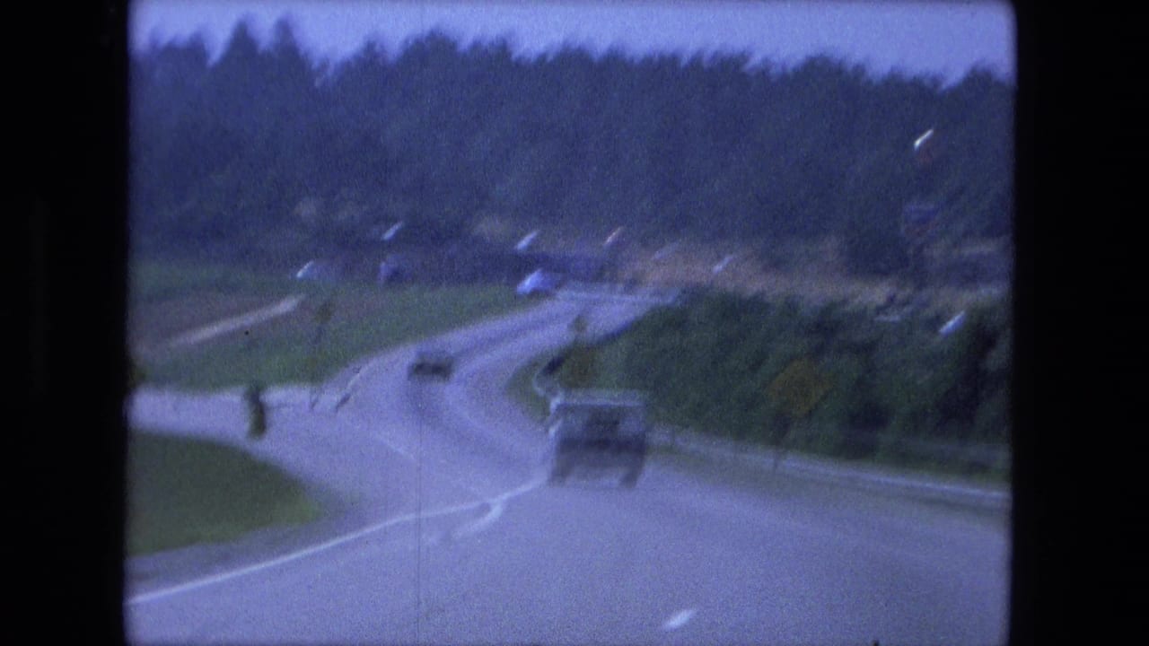 Highway curve with a boxy vehicle ahead, several cars in the distance, and wooded roadside.