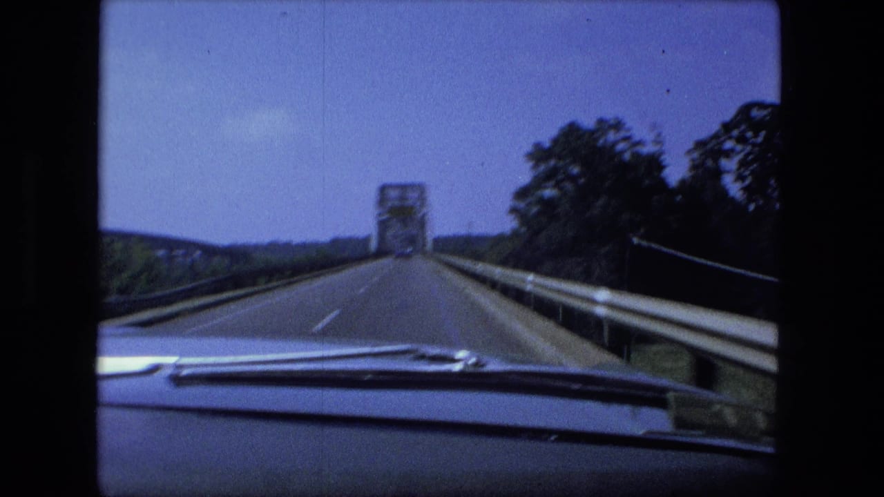 A Fort Wayne road scene from inside a moving car, with windshield wipers at the bottom and a steel truss bridge ahead under a blue sky.