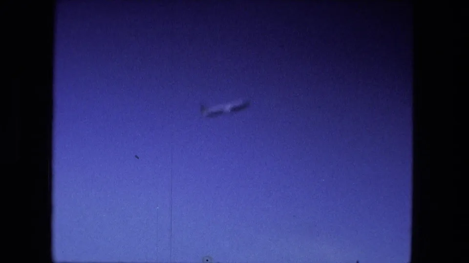 A distant airplane appears against a saturated blue sky in 1974 8mm home-movie footage from the Fort Wayne, Indiana reel.