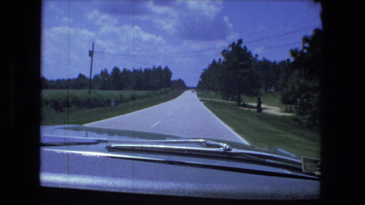 Forward view from inside or near a car traveling along a rural road in the Fort Wayne, Indiana area, with hood and windshield wipers visible.