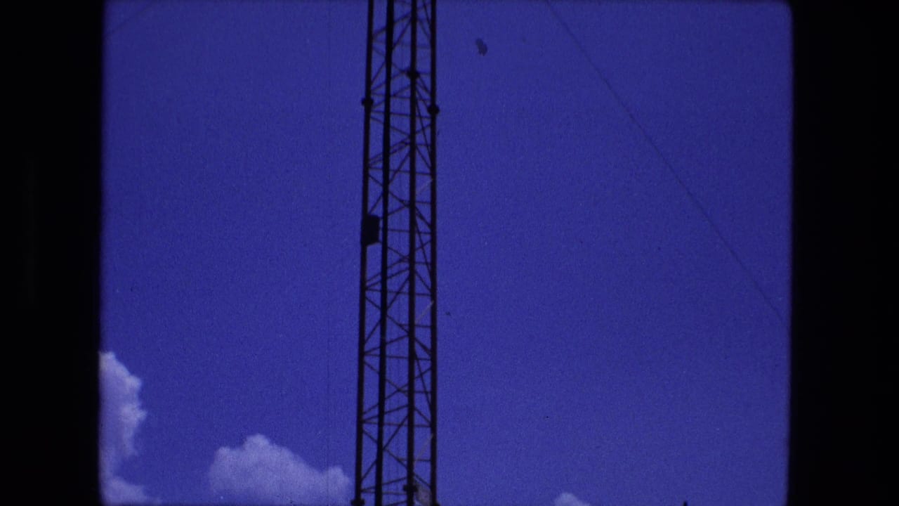 1974 Fort Wayne home-movie frame with the tower shifted to the left of center, showing wires, blue sky, and small clouds.