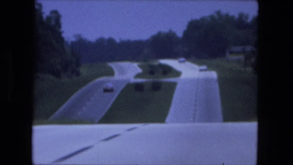 1974 home-movie view of a divided interstate near Fort Wayne, with the road curving through green terrain and a few distant vehicles.