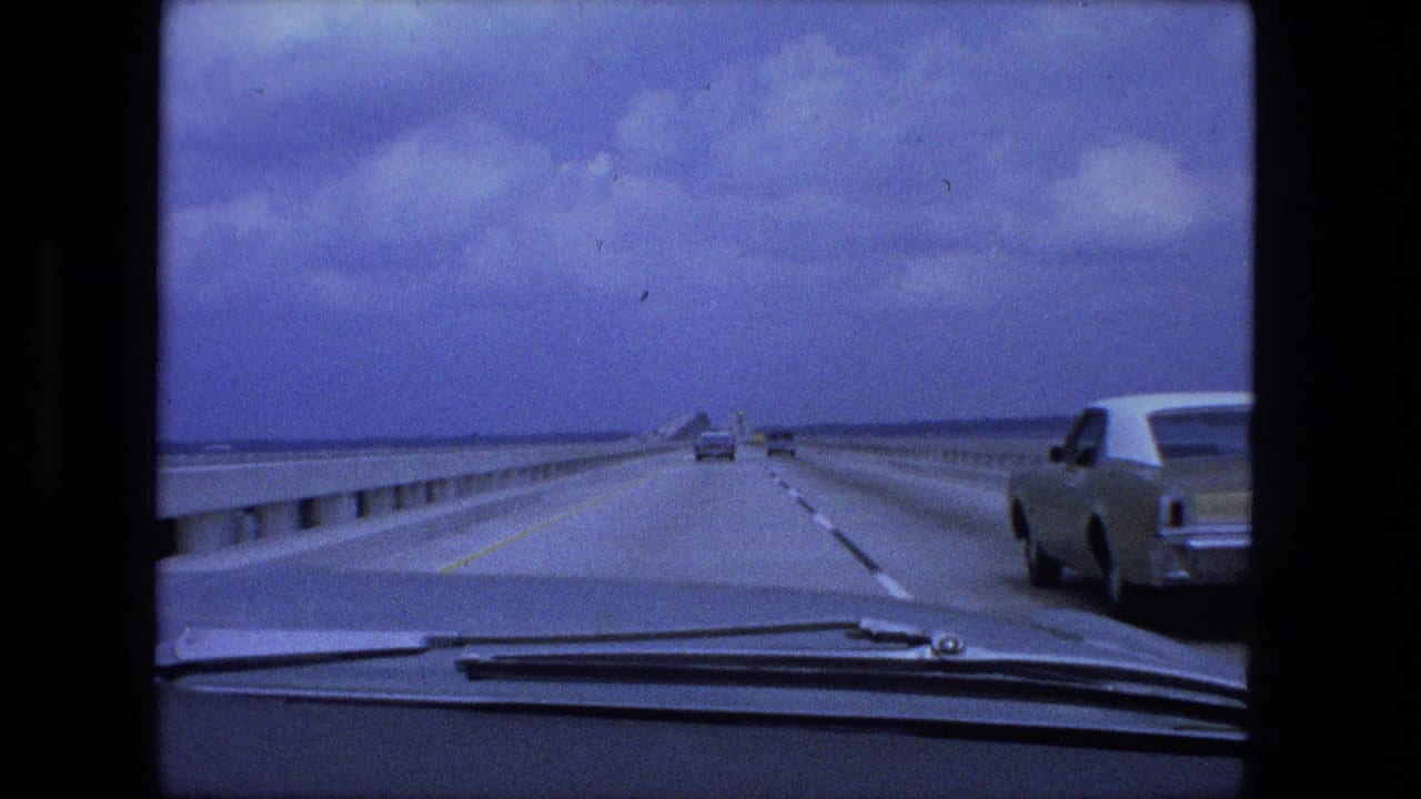 Car windshield view along a multi-lane bridge roadway under a cloudy sky.