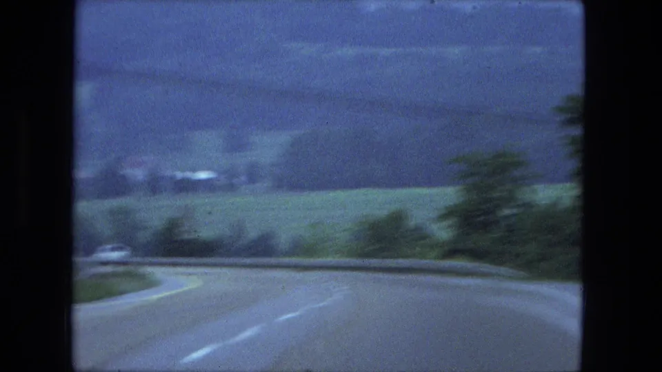 Soft 8mm road frame from the Fort Wayne area, showing a curving highway bordered by green fields and trees.