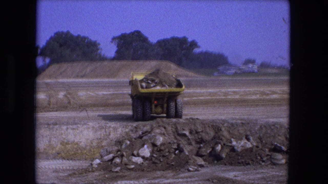 Yellow dumper truck approaches a dirt pile at an open construction site.
