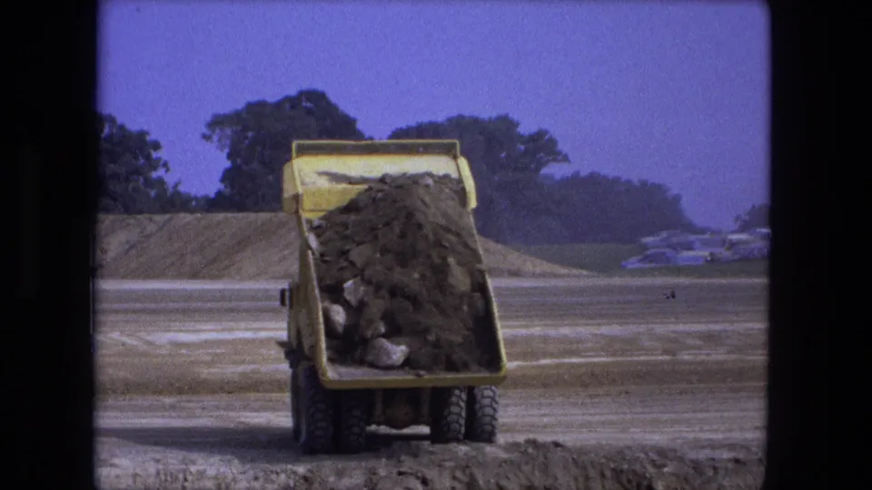 The yellow dumper truck continues unloading its dirt and rock load into the hole at the Fort Wayne construction site.