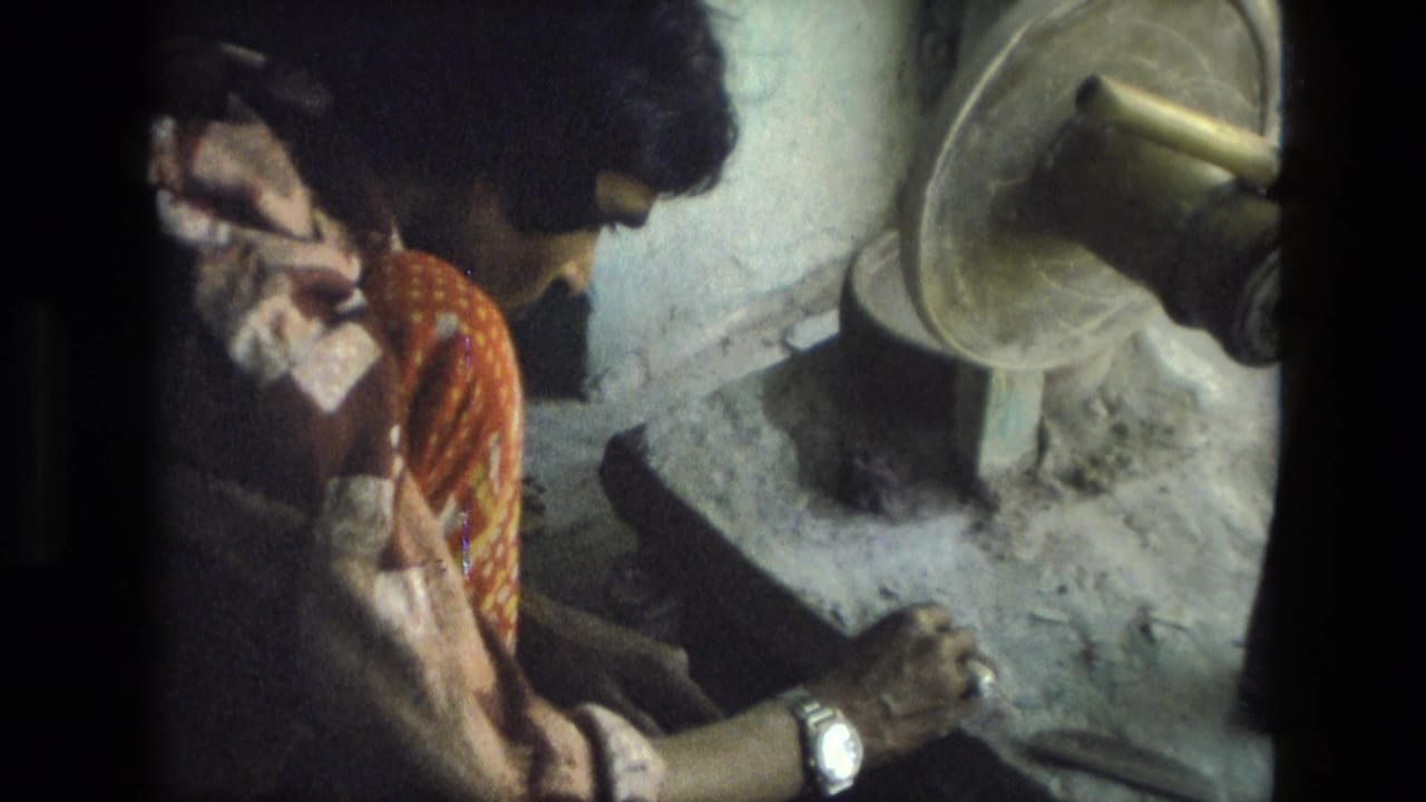 Seated artisan leans over a work surface with a grinding wheel visible nearby.