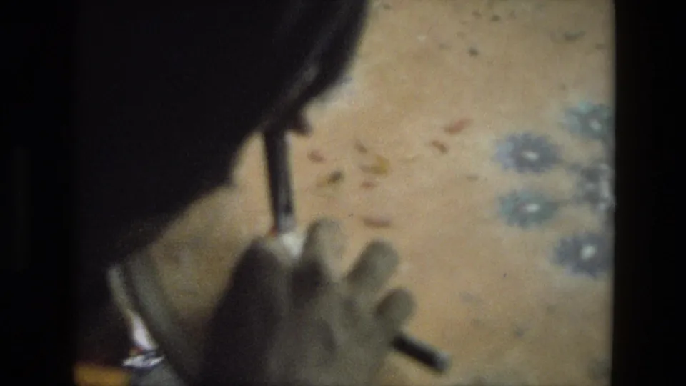 Close 8mm view from India, 1974, showing the artisan's hands and tool near a patterned floor surface.