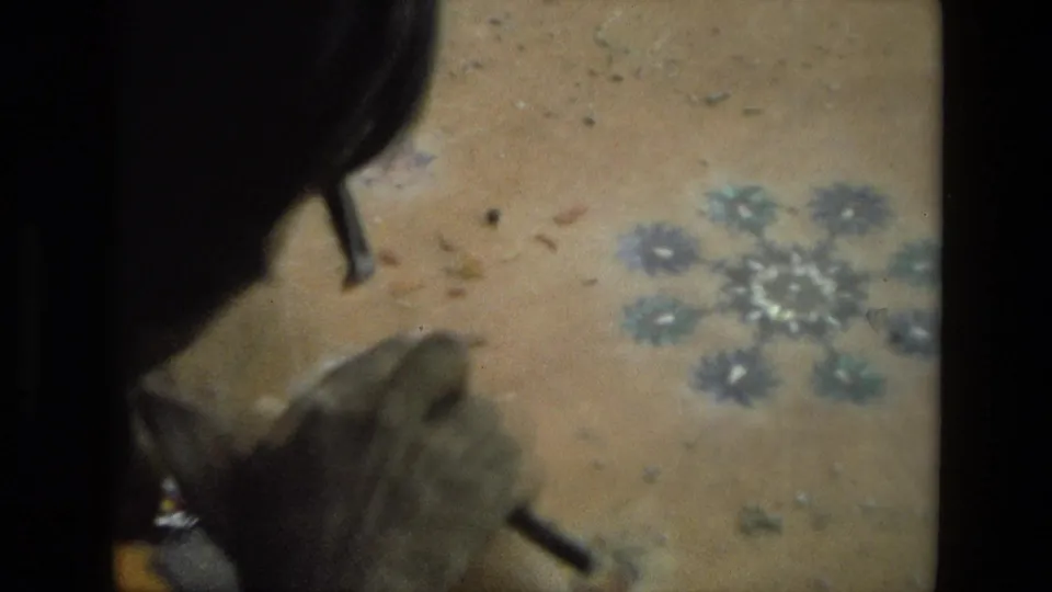 The final frame keeps focus on the artisan's hand work, with a tool, dusty floor, and floral pattern visible in the 1974 India footage.