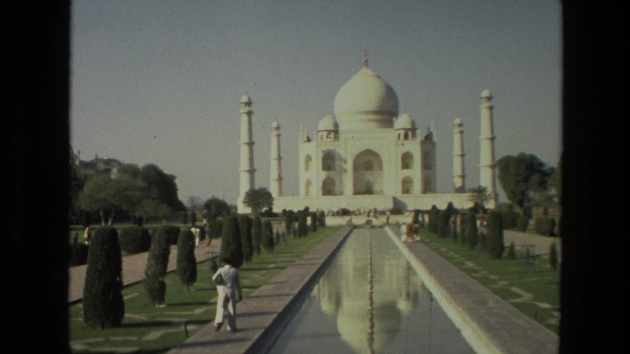 Taj Mahal seen across a reflecting pool with gardens and a visitor walking along the path.
