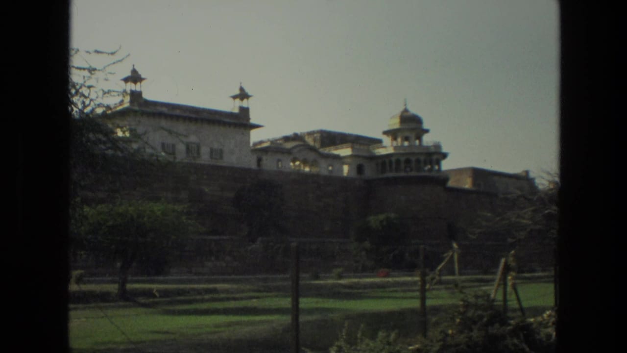Historic fort wall and domed pavilions seen beyond lawns through a dark vertical frame.