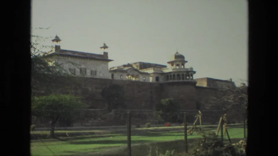 1974 India home-movie view of a historic fort exterior, with domed architecture above a long stone wall and garden areas below.