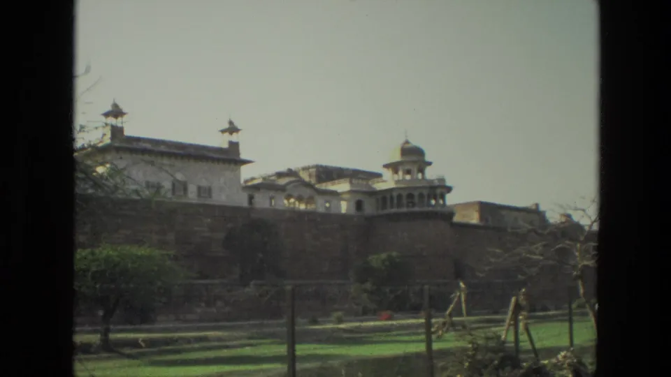 1974 India travel frame of a fort-like historic exterior, with a domed pavilion above a stone wall and landscaped grounds in front.