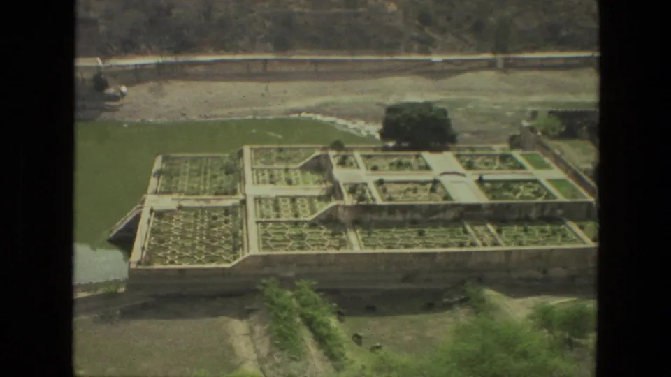 1974 India travel footage frame with geometric planting beds, walkways, pond water, trees, and a road at the top of the view.