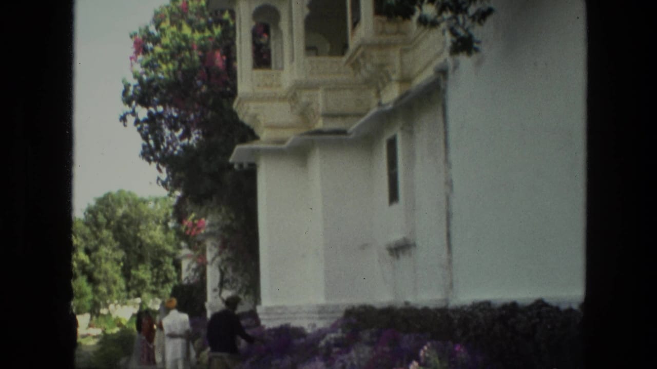 Visitors stand near an ornate white building and flower-lined garden path.