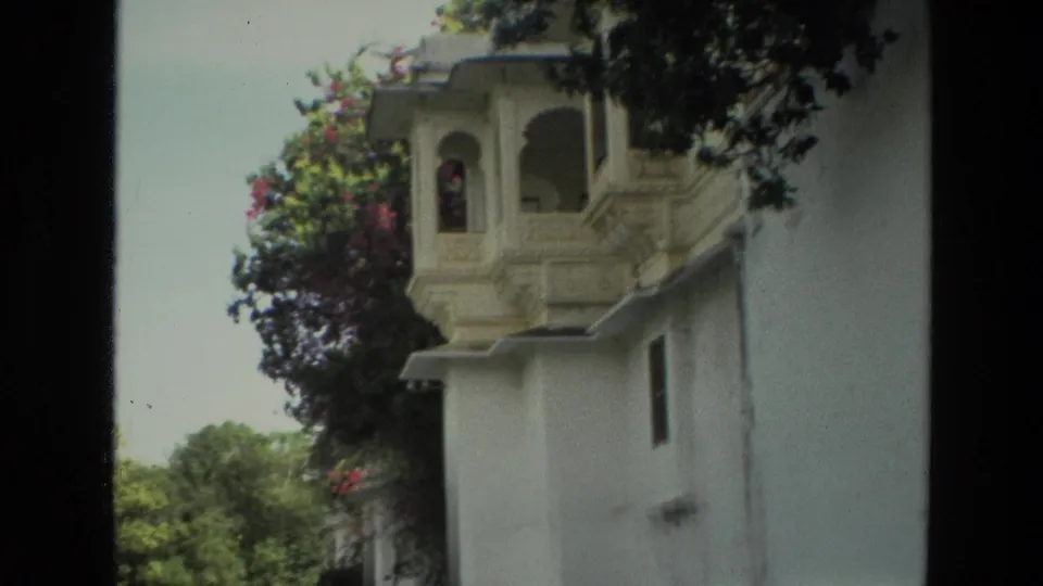 1974 India home-movie view of an ornate white building facade above trees and flowering vines.