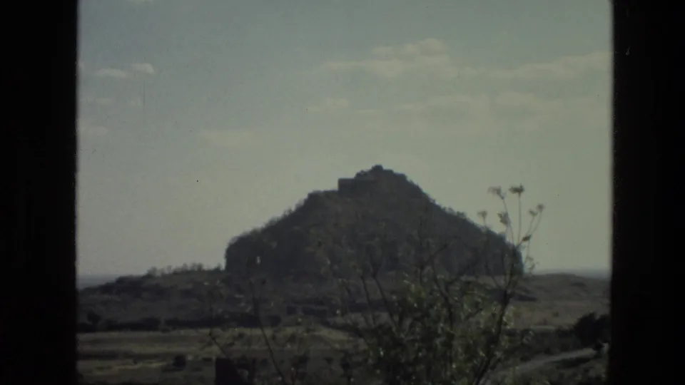 1974 India 8mm view of a rugged hill with a small structure near the top, seen across dry scrub and open terrain.