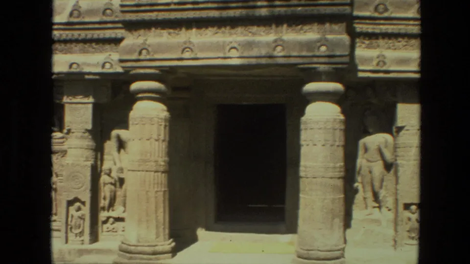 1974 India 8mm frame showing a carved stone temple facade with columns, a dark doorway, and sculpted relief figures.