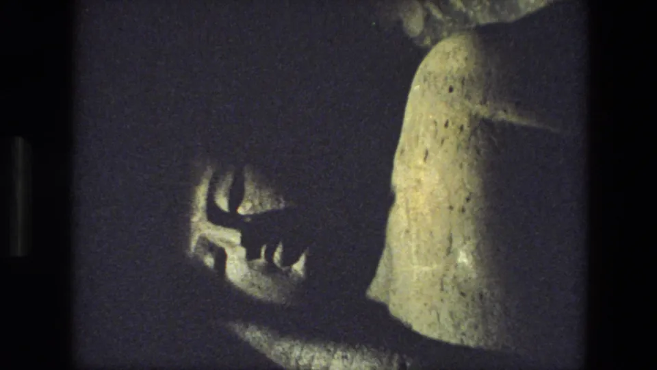 1974 India 8mm frame showing a low-light interior temple detail with a carved shadow form and pale weathered stone.
