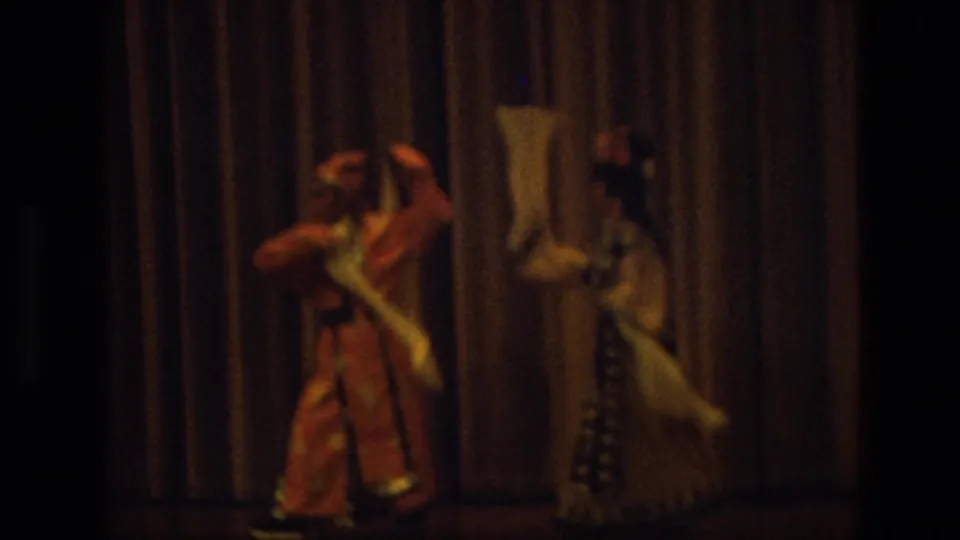 1974 India 8mm frame showing two traditional-costumed performers dancing with white scarves against a heavy curtain.