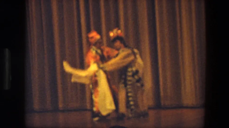 A close stage moment from 1974 India 8mm footage, with two costumed dancers and a white scarf in motion.