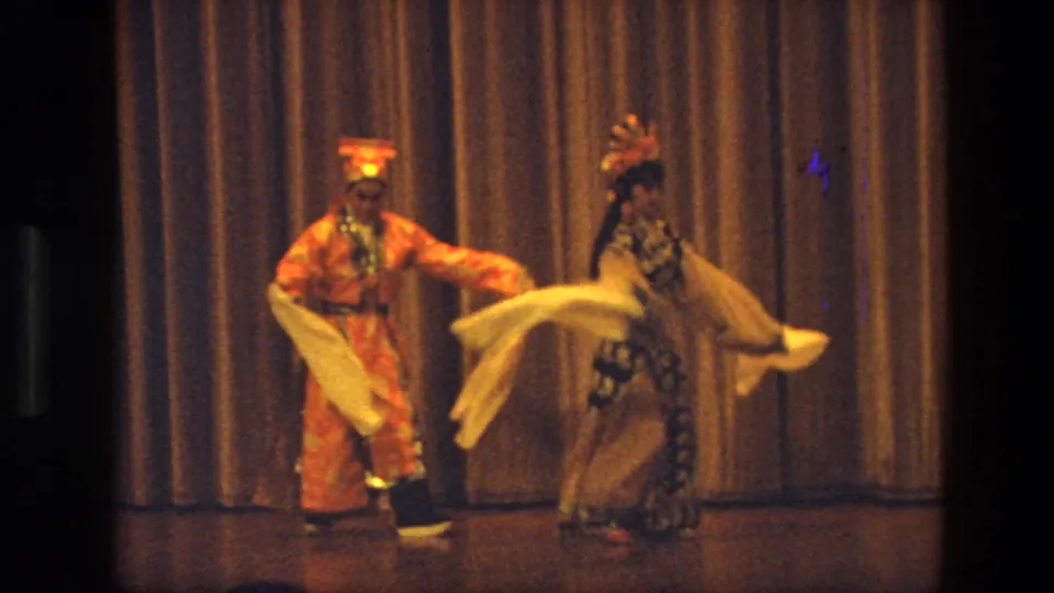 1974 India home-movie frame of two stage dancers separated across the frame, each holding a white scarf.
