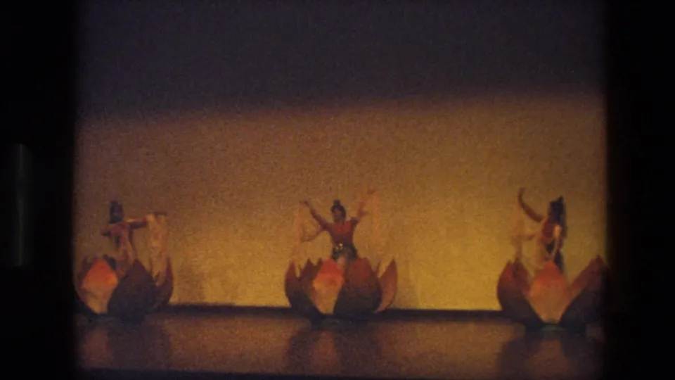 Three costumed performers appear spaced across the stage in India in 1974, each near a lotus-shaped prop.