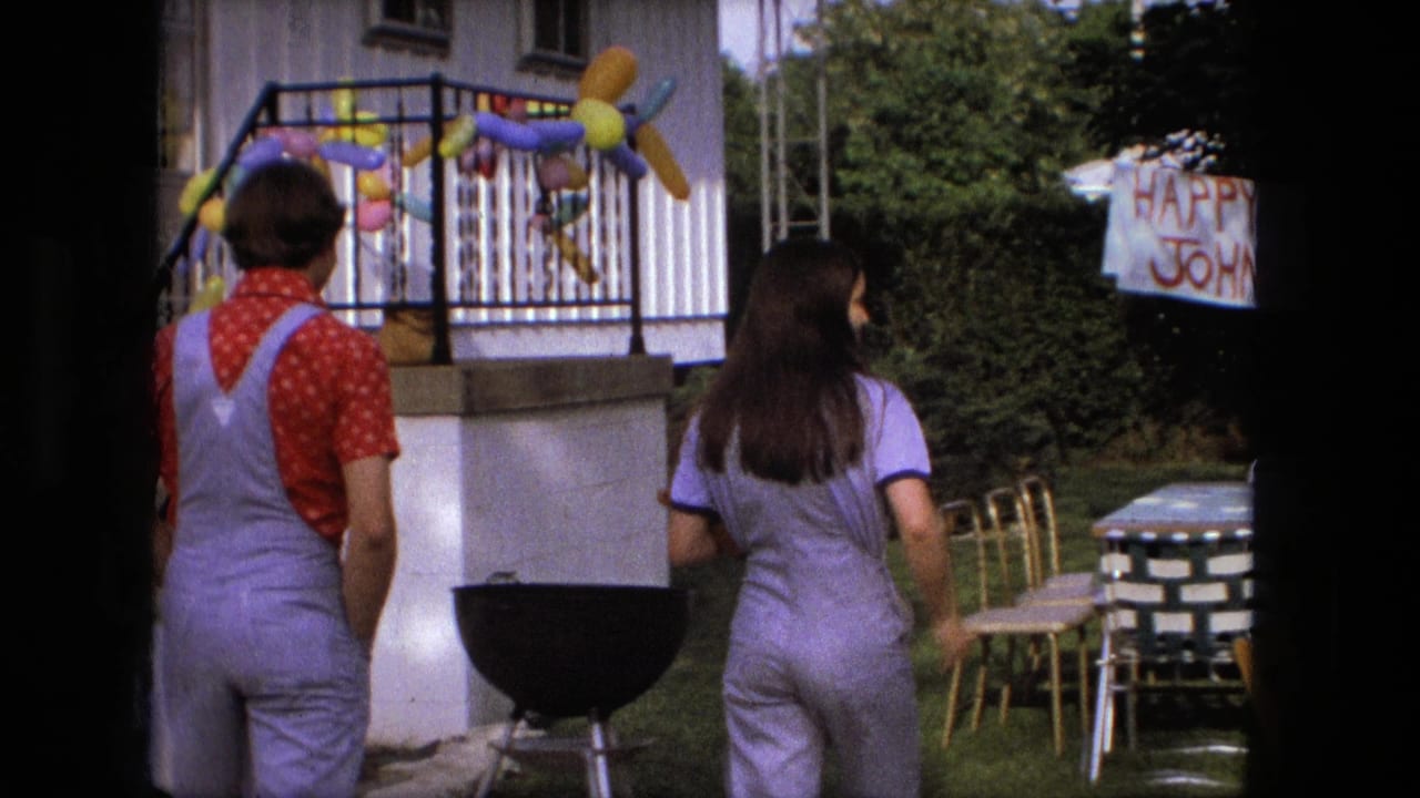 Man in overalls and woman in purple walk beside a porch decorated with balloons.