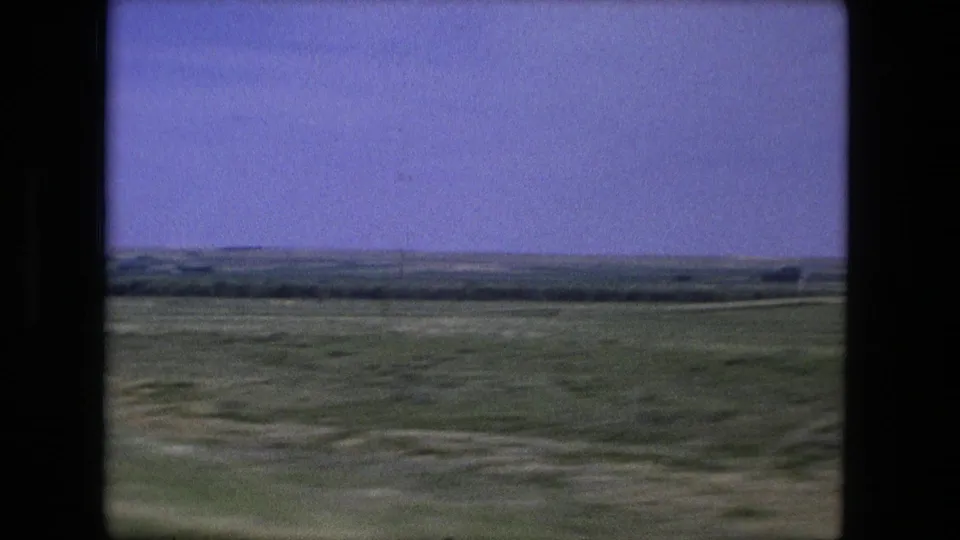 1976 Fort Wayne-area countryside with green fields, a low horizon, pale sky, and dark frame edges from a moving vehicle view.