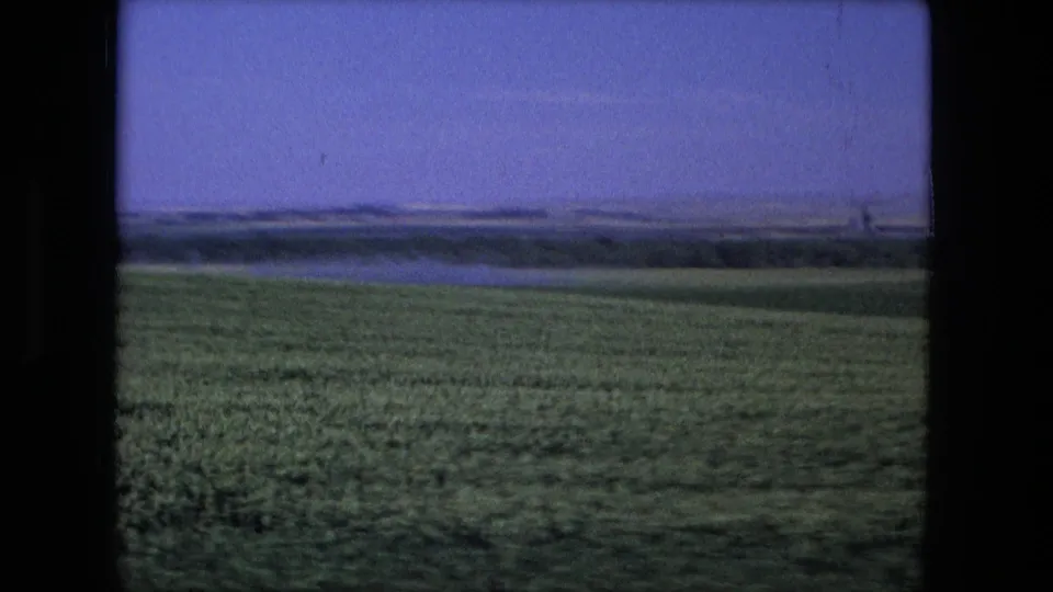 Green cultivated land and a distant rural horizon appear in this 1976 Fort Wayne-area moving-vehicle landscape frame.