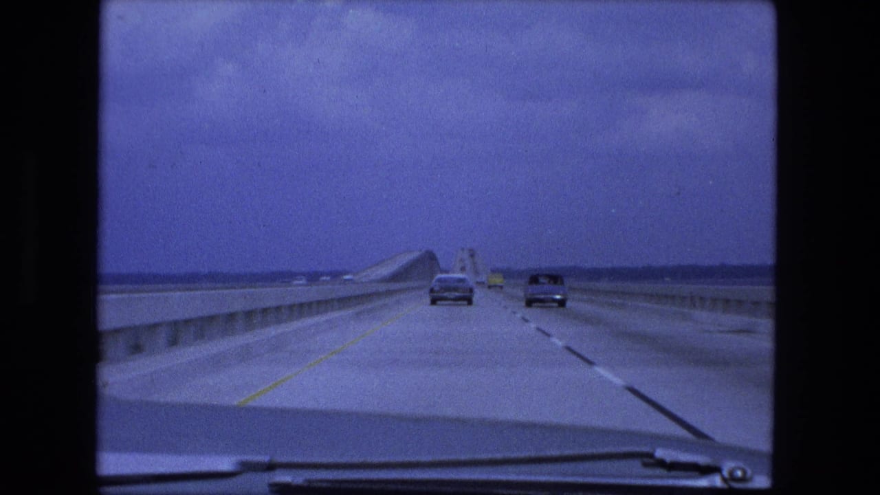 Driver view on a bridge highway with cars ahead and windshield wipers at the bottom of frame.