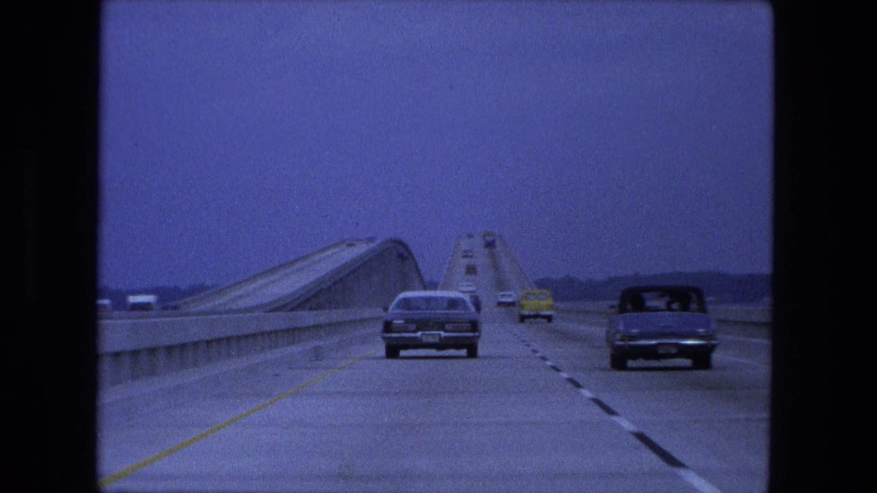 Cars pass along a divided bridge highway with a raised bridge span visible ahead.