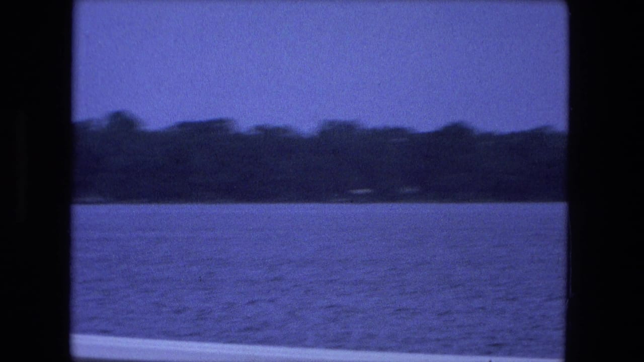 1974 Fort Wayne 8mm frame with open water, a wooded far shore, blue sky, and visible film gate edges.