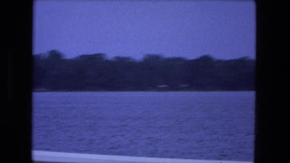 1974 Fort Wayne 8mm frame with open water, a wooded far shore, blue sky, and visible film gate edges.