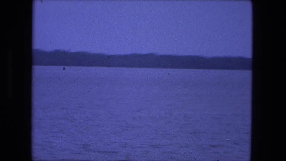 1974 Fort Wayne 8mm frame showing calm water and a distant wooded horizon with blue color cast and gate edges.