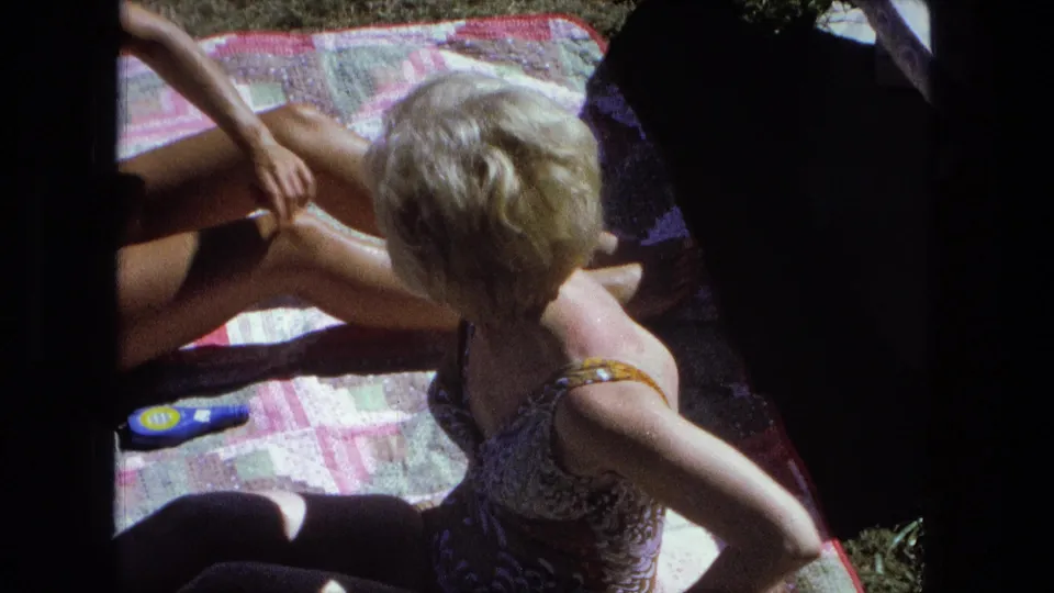 A woman in a patterned swimsuit sits facing away on the patchwork blanket, with another sunbather partly visible in Fort Wayne, Indiana.