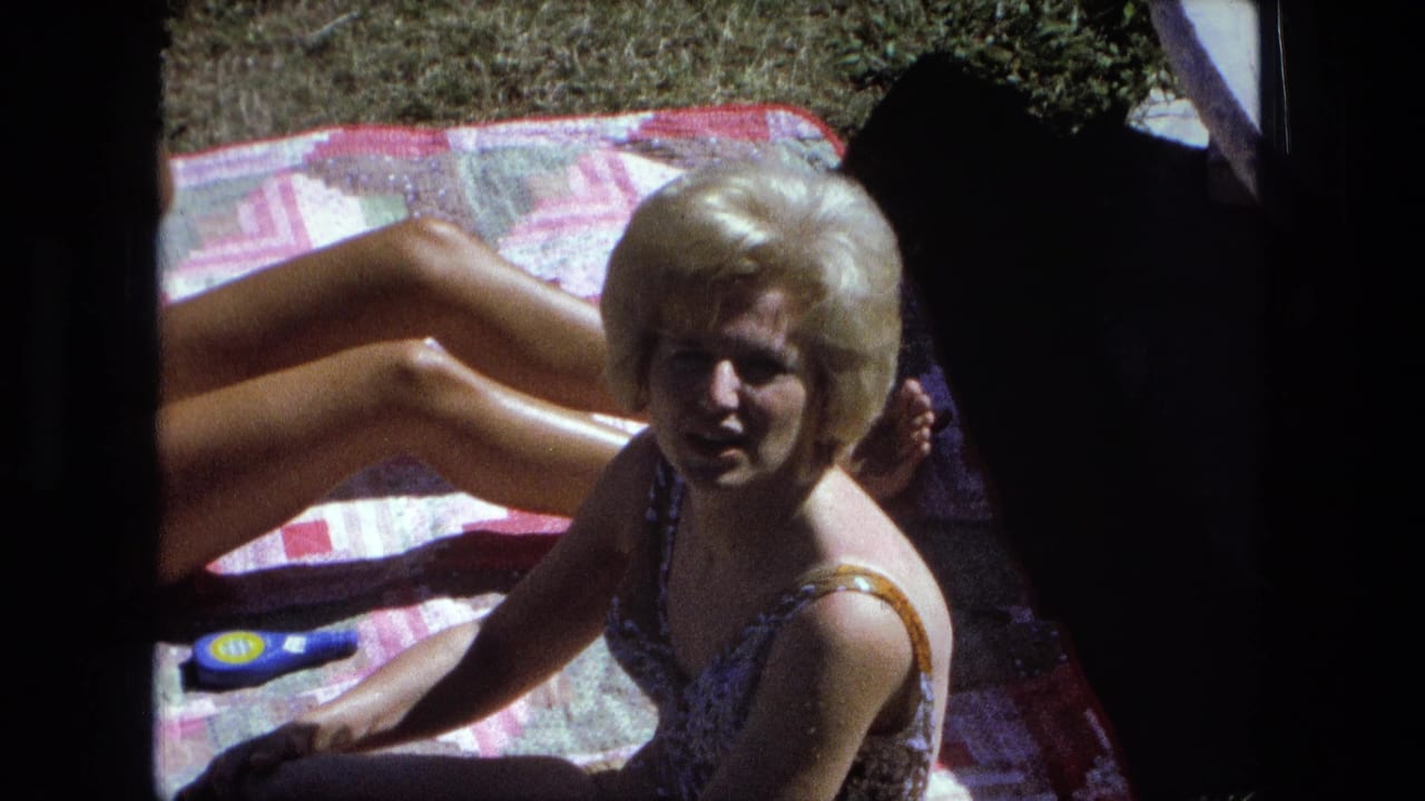 Blonde woman in a swimsuit sits on a patterned blanket in bright sun.