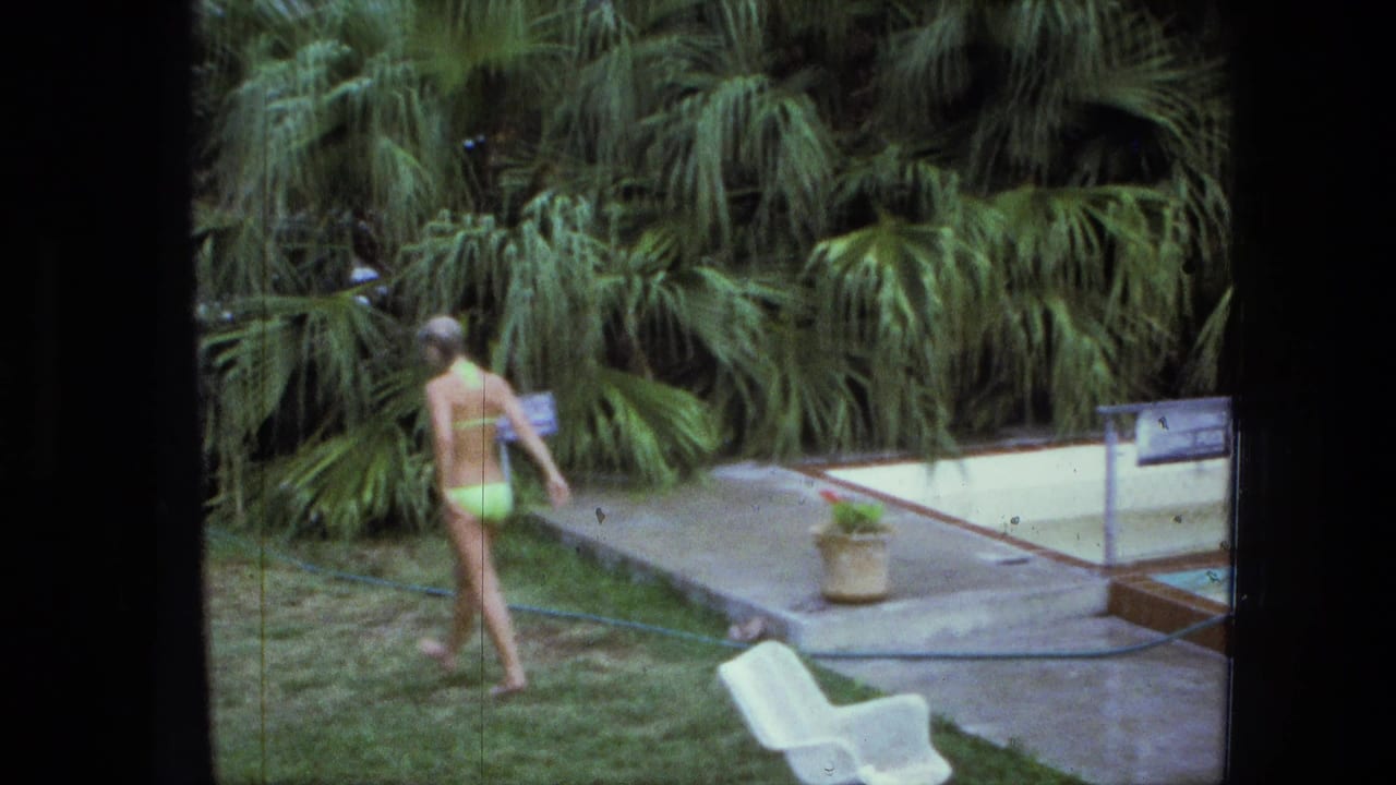 A woman in a green bikini walks toward the backyard pool area, with dense palms or tropical-looking plants behind the deck.