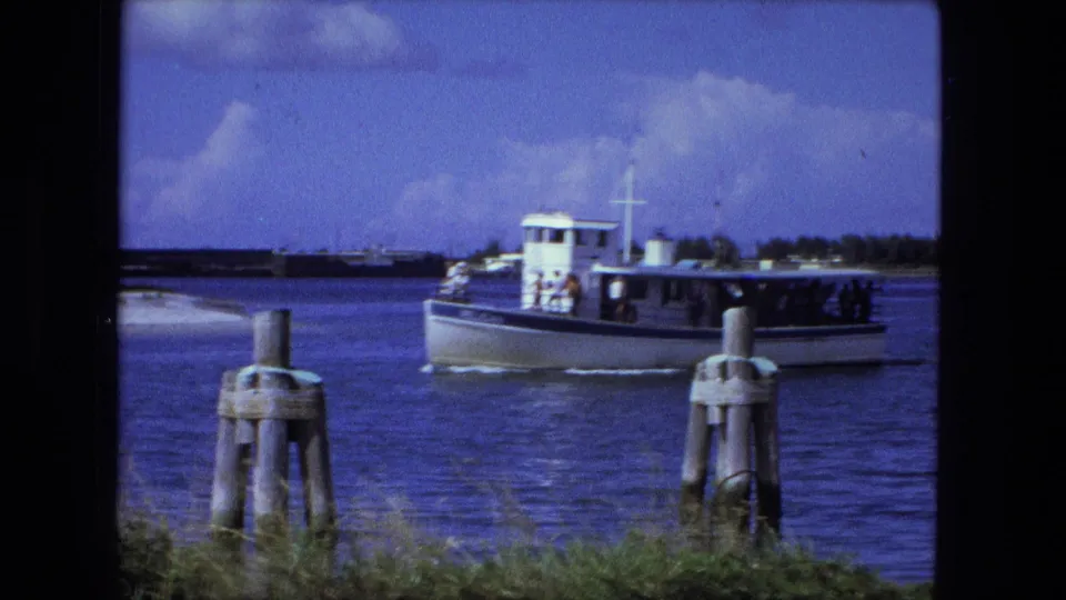 A white passenger boat glides past two wooden pilings in 1974 Fort Wayne home-movie footage, with passengers visible along the side.