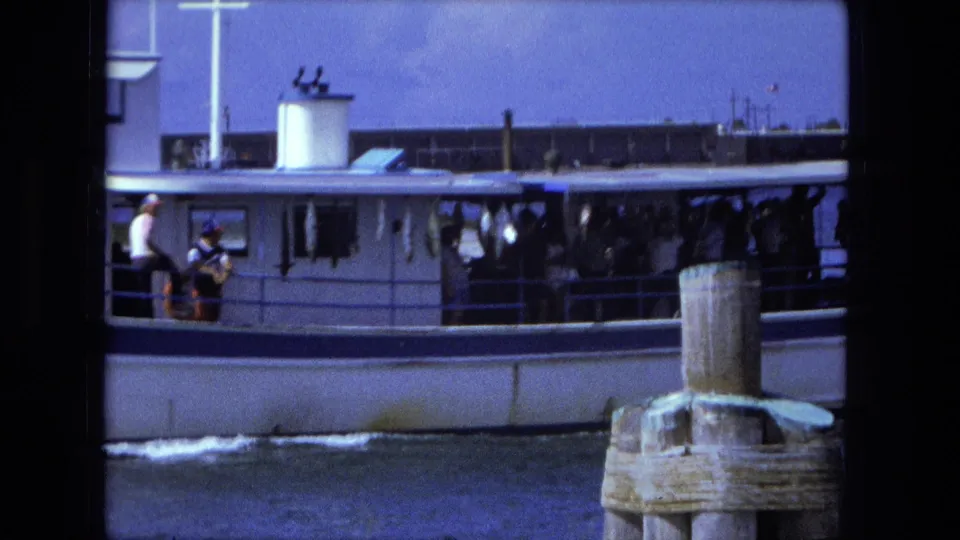 Side view of the white passenger boat on Fort Wayne waters, with riders along the deck and a wooden piling in the foreground.