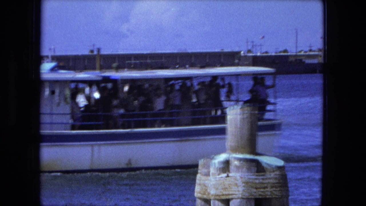 Crowded white ferry passes wooden pilings on blue water.