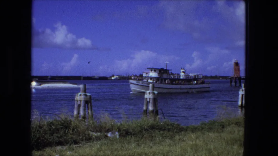 The white passenger boat continues across the water in this 1974 home-movie frame, with passengers visible as small figures on deck.