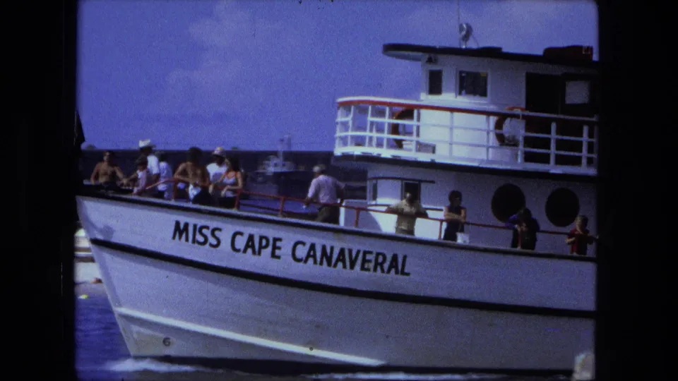 Close side frame of the Miss Cape Canaveral passenger boat, showing riders along the rail and the vessel name on the hull.