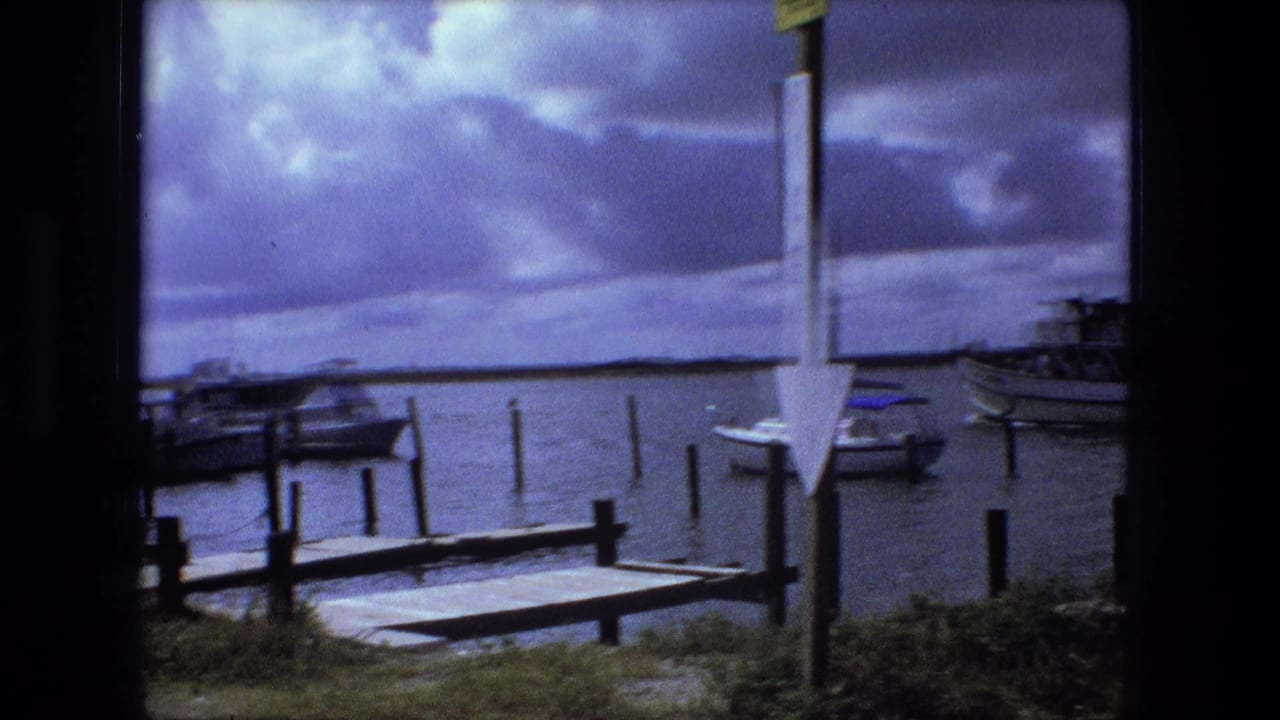 Docked boats and wooden piers seen through a dark window frame under a cloudy sky.