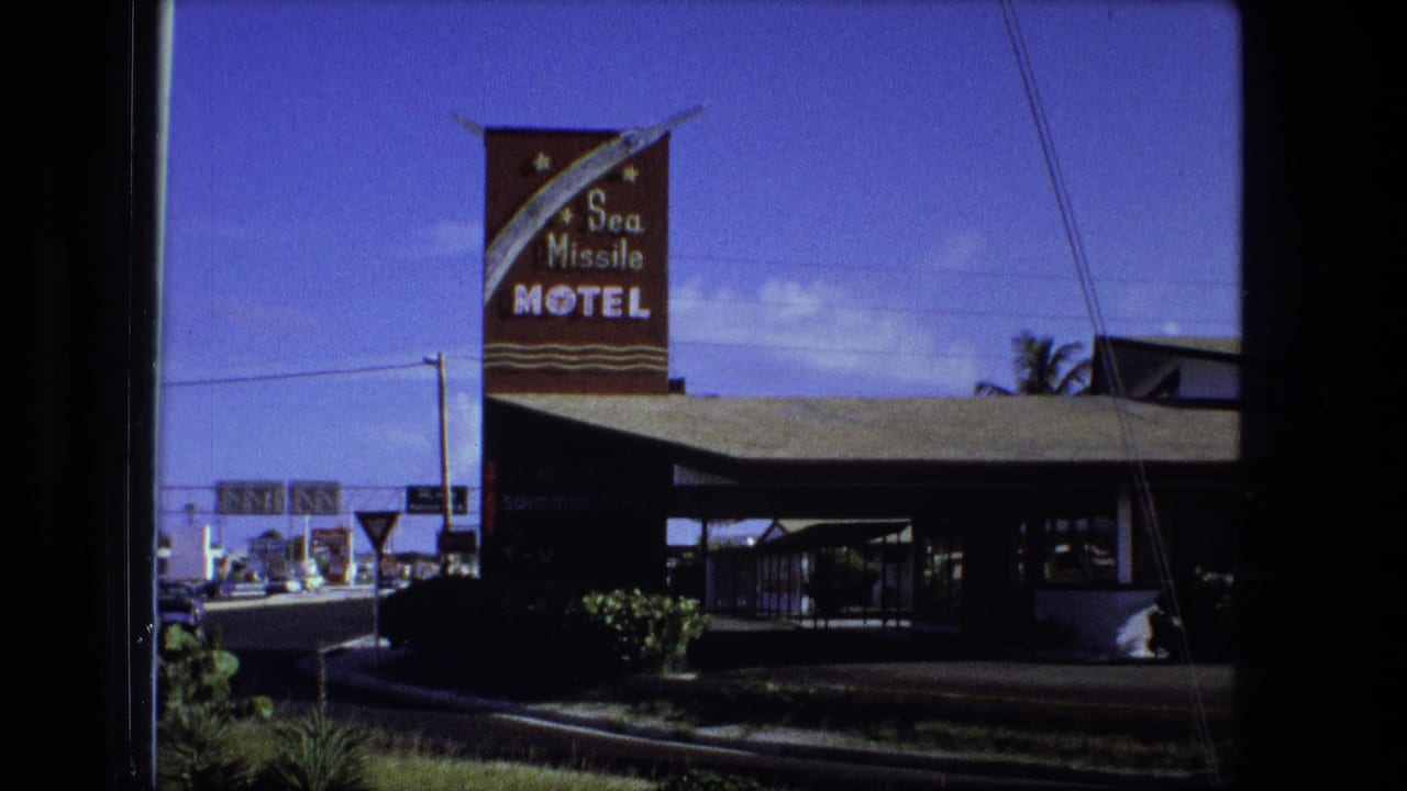 Roadside motel exterior with a Sea Missile Motel sign, canopy, hedges, and blue sky.