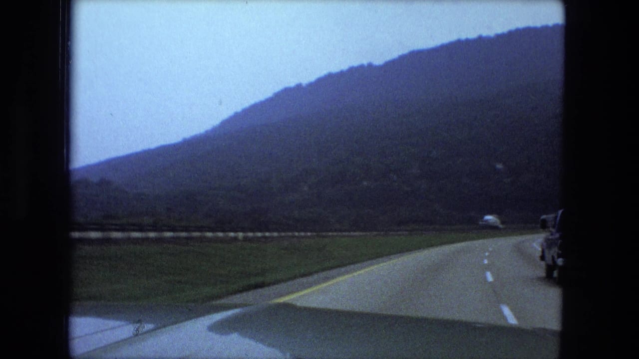 Highway curving through hills with a vehicle edge visible at the right.