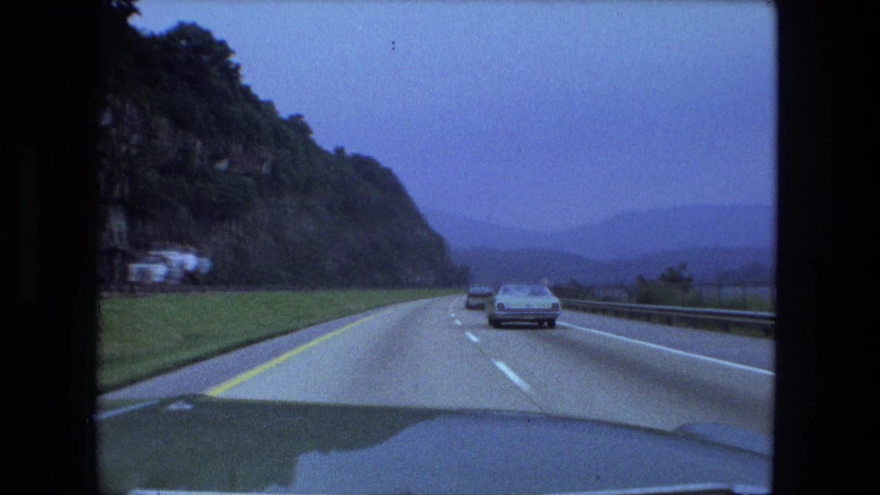Cars travel along a highway with a rocky cliff on the left and water to the right.