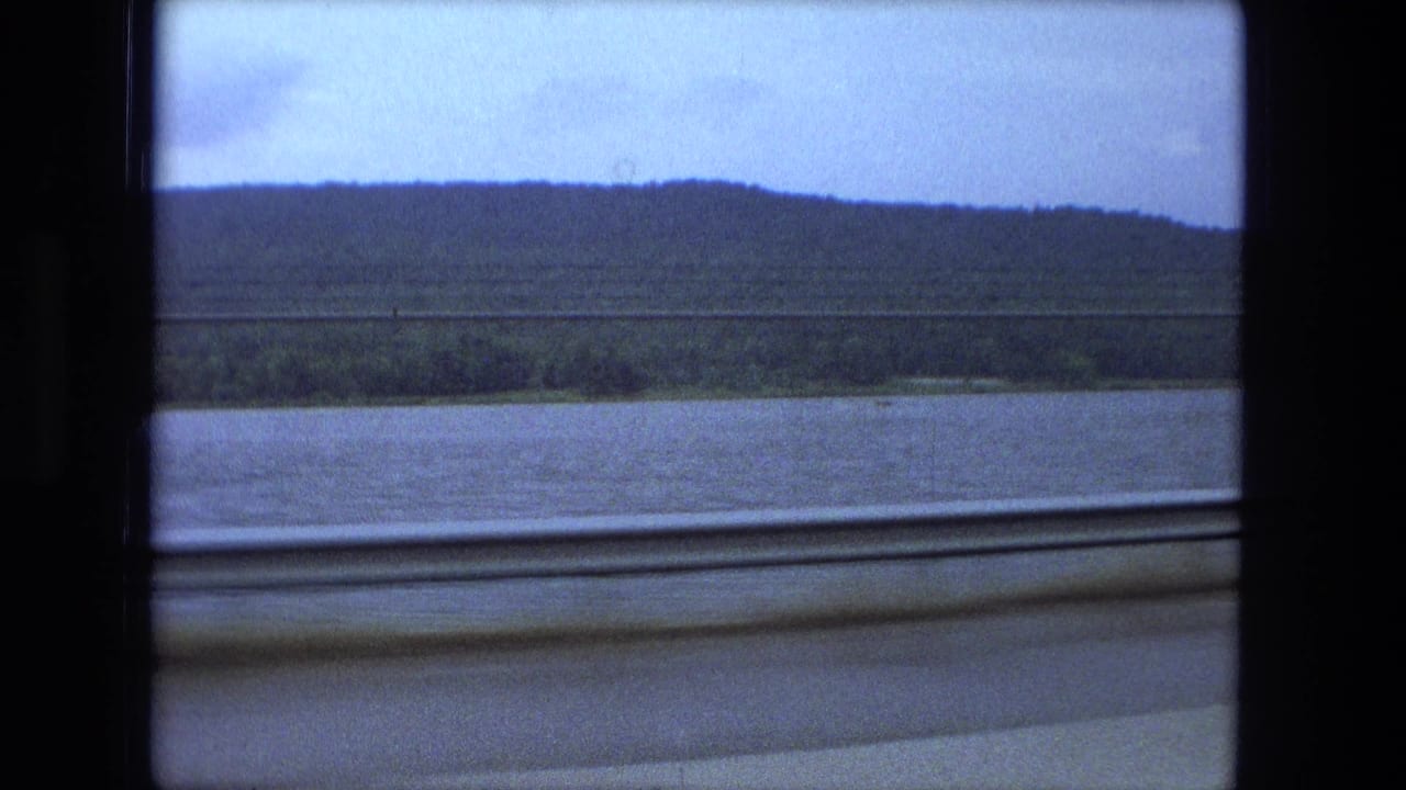 Wide river below a dark ridge, framed by the train window.